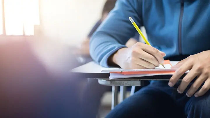 Estudante escrevendo na carteira com lápis amarelo